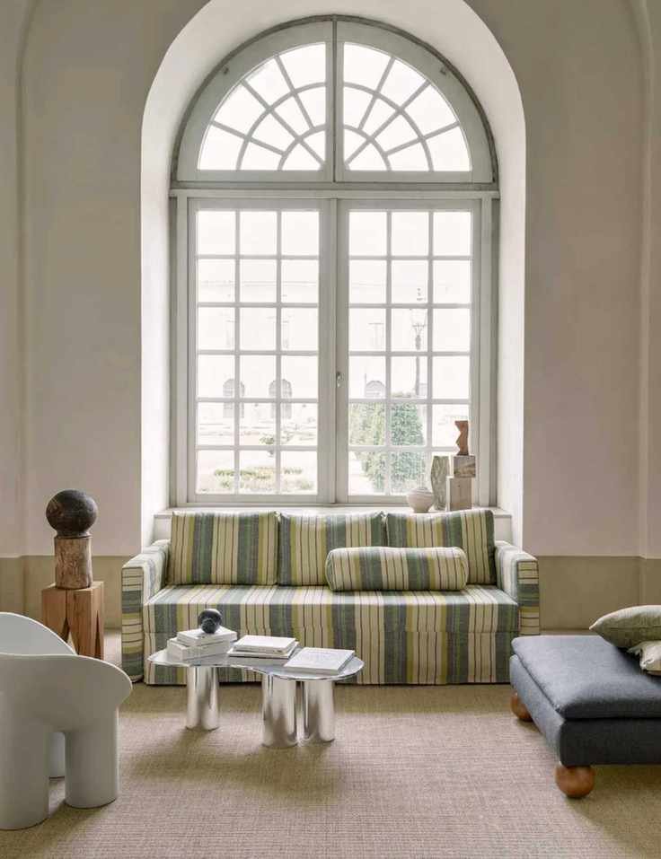 Modern living room design in traditional interior, sofa with striped upholstered covers, armchairs and lounge chairs working with sofa to create a sociable seat space, large arch window
