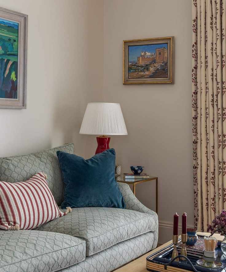 The corner of a living room with creamy beige walls painted in Slipper Satin by Farrow &amp;amp; Ball, featuring a blue sofa and decorative items.