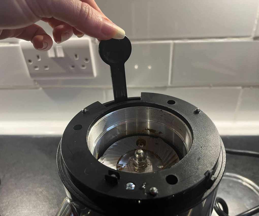 Fingers picking the Aarke Coffee Grinder cleaning brush from its compartment beside the burrs