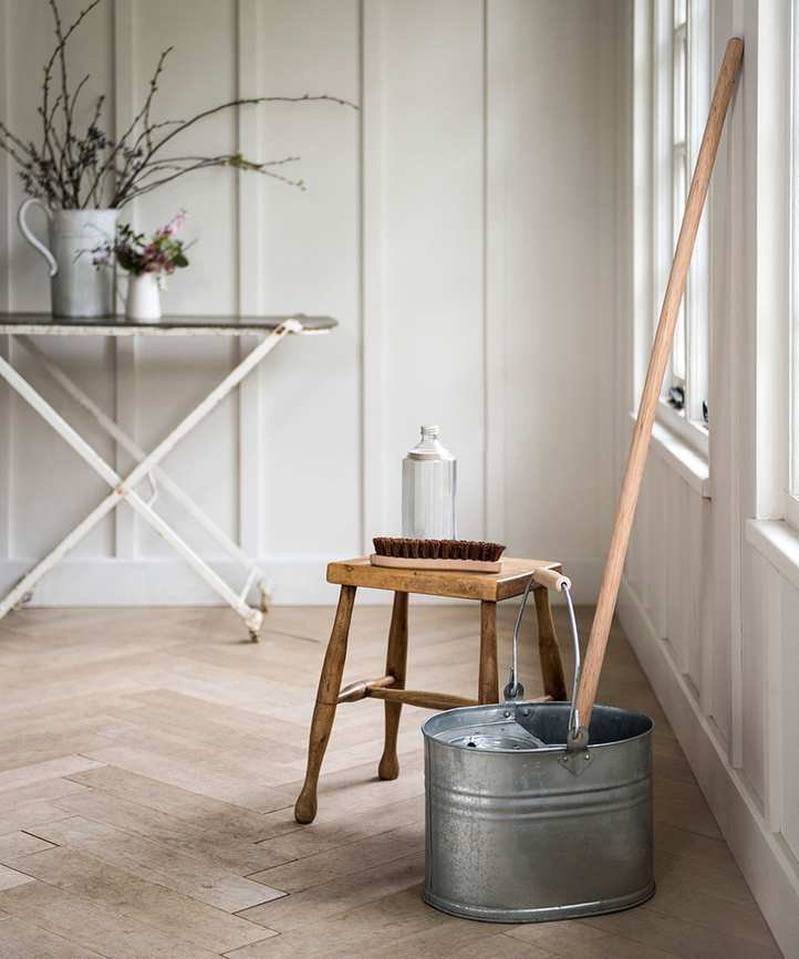 A mop standing in a metal bucket against a wall