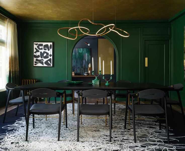 green dining room with black table and large gold ceiling light hanging over it