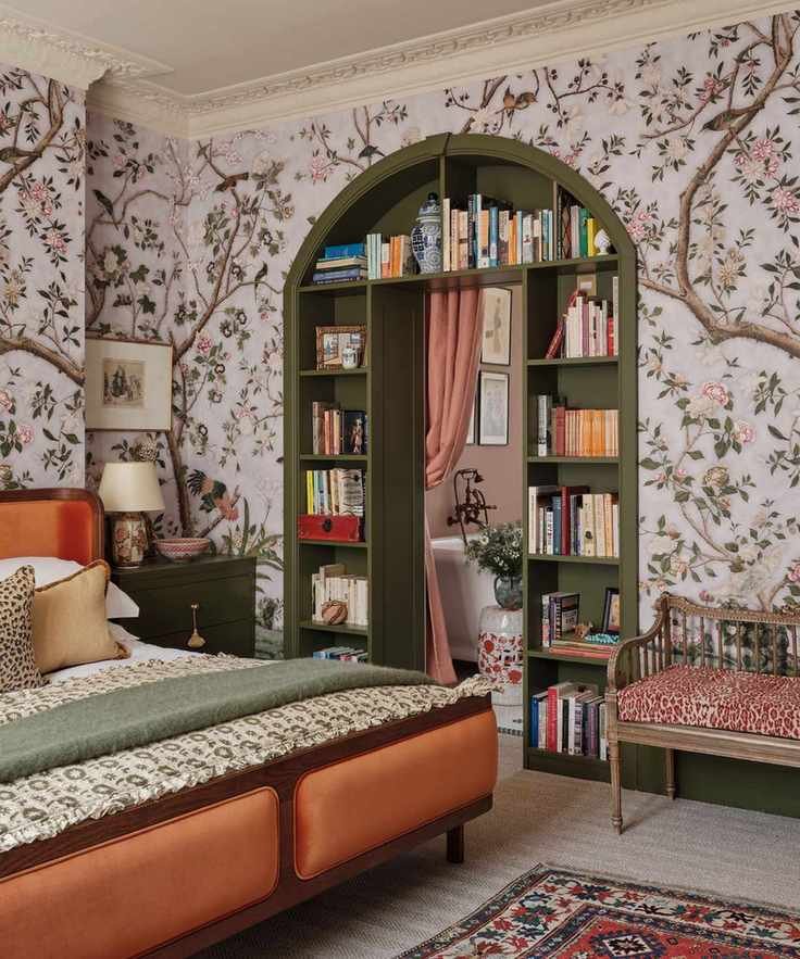 floral mural wallpaper in a bedroom with a door into the utility built with dark green bookcase shelving, a pink drape and an orange bed