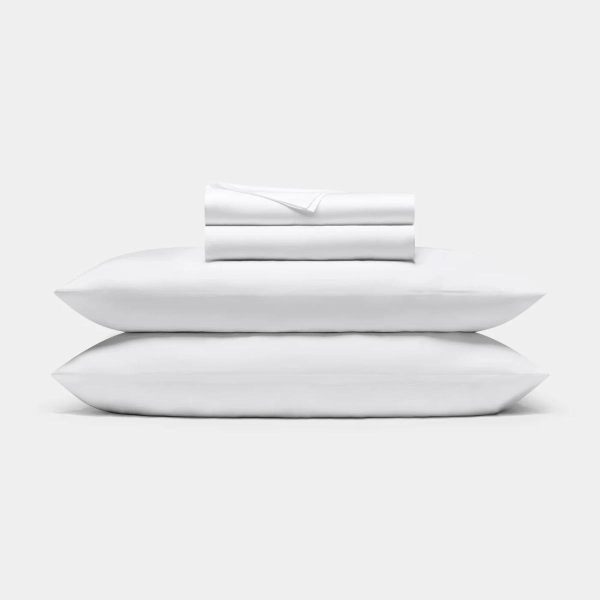 A white pillowcases shown on two piled pillows with folded sheets on top.