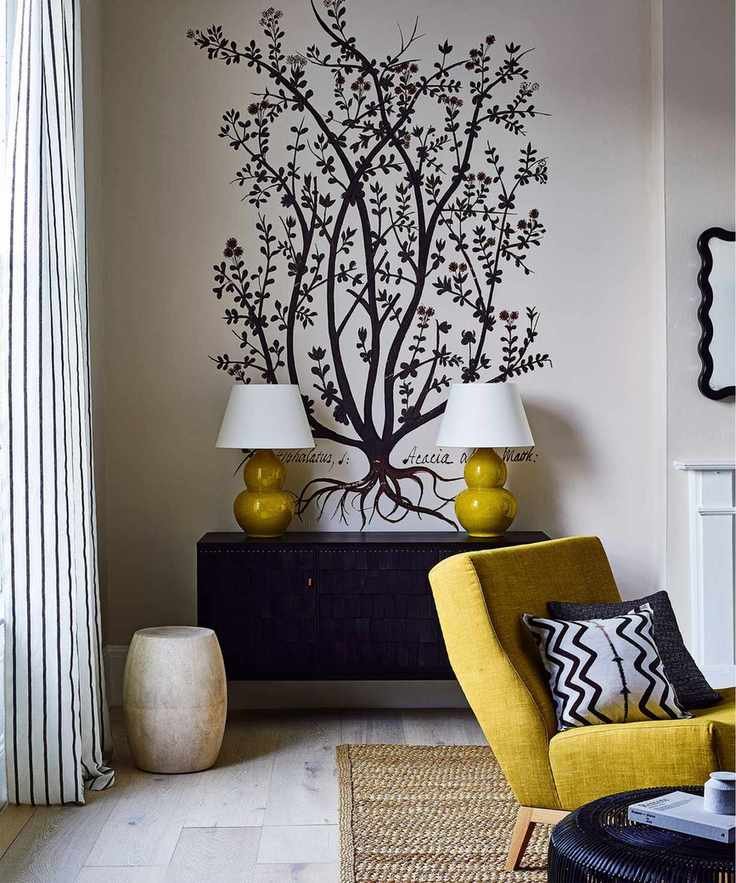 A living room showcasing a yellow armchair and lamps against a white wall with a black tree design