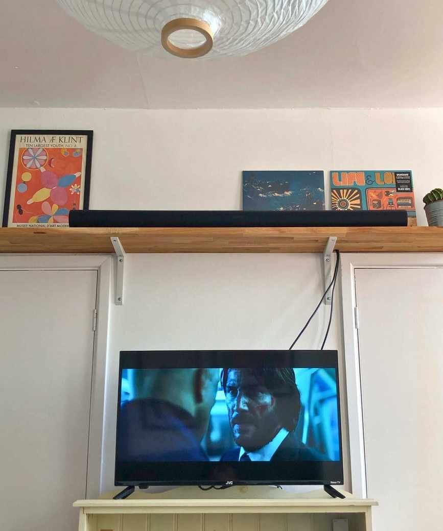 Sonos Arc Ultra soundbar in Dan Fauzi's home, on wooden shelf with cactus plant, above TV showing John Wick: Chapter 2.