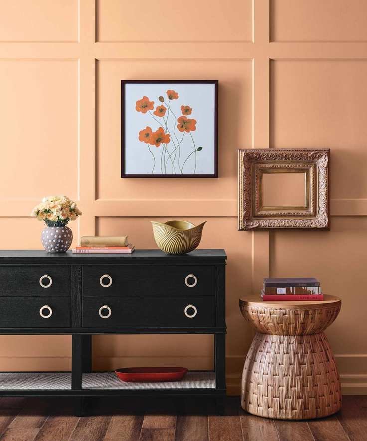 Entryway with orange walls, rattan stool, black console and art on walls