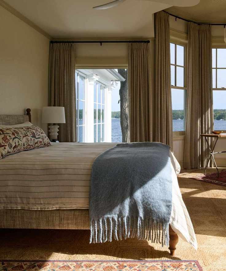 A bedroom with a neutral color scheme and large windows with a powder blue throw on the bed.
