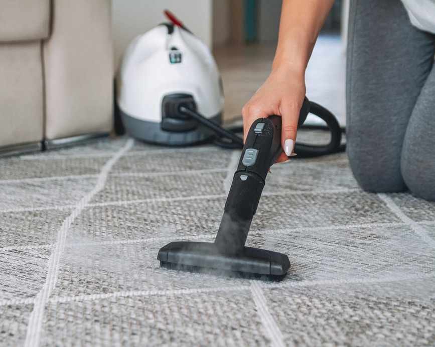Woman cleaning a grey, low-pile carpet with a steam cleaner