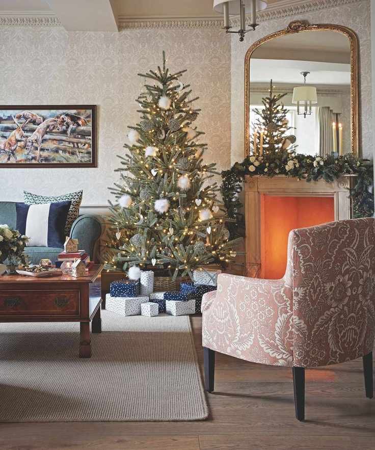 A cozy Christmas living room with a Christmas tree, lit fire in the fireplace, upholstered chair, rug, wooden coffee table and blue sofa.