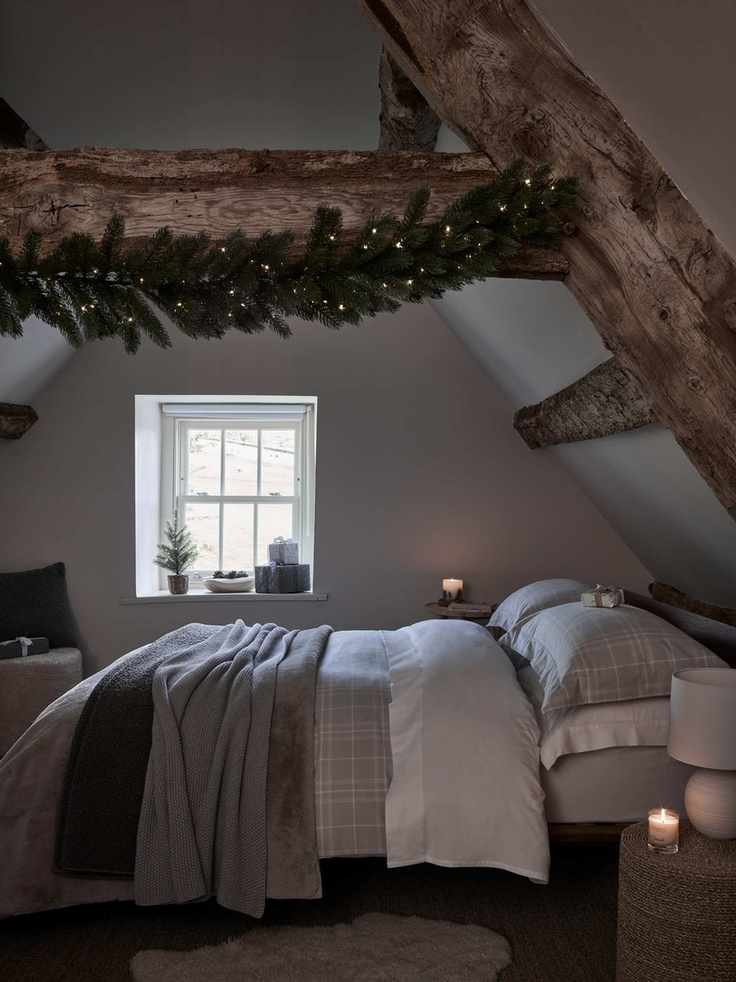 Christmas bedroom decor with garland on a beam, gray bedding, rug, basket style side table, lamp, mini Christmas tree