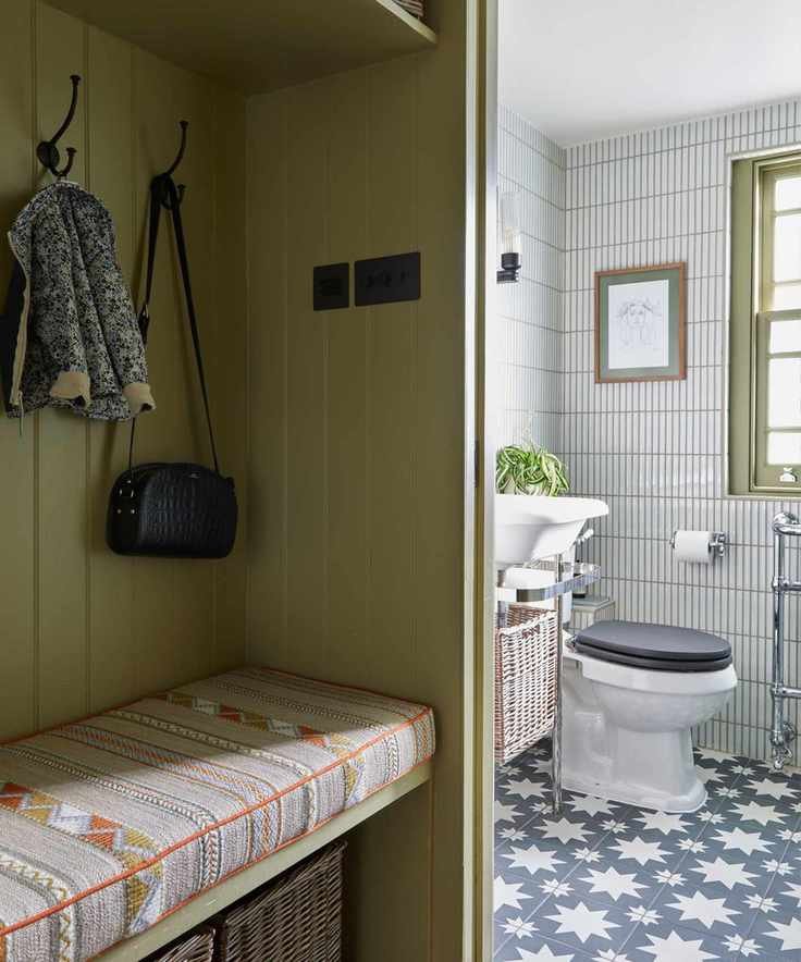 A bathroom with blue patterned tile on the floor and white vertical tile on the walls, with a view from an olive green room