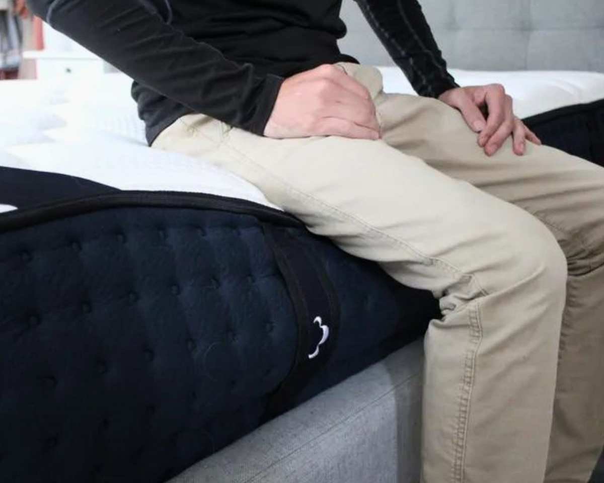 A close-up of a man sitting on the DreamCloud Classic Hybrid Mattress.