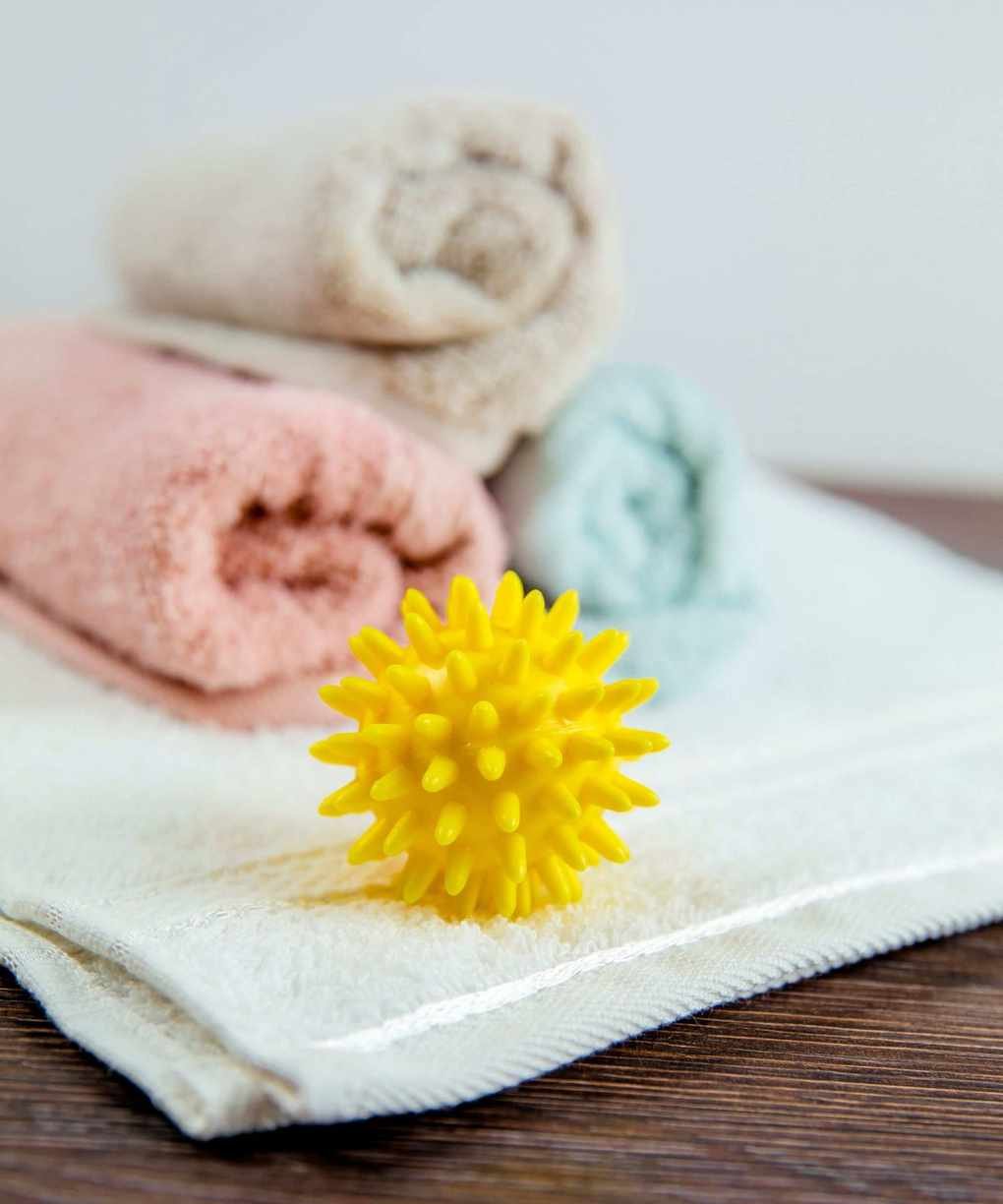 A plastic dryer ball on a white towel in front of a stack of colorful towels