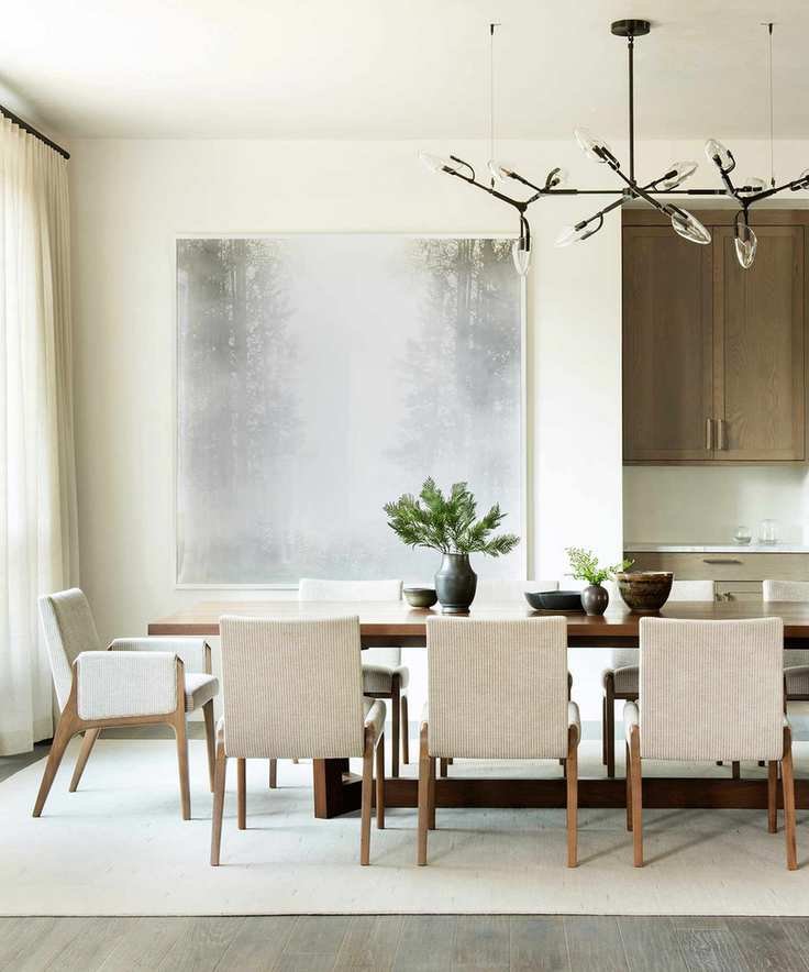 Dining room with wood floor and ivory area rug, white walls, ivory upholstered dining chairs, dining table, pendant light and large abstract artwork