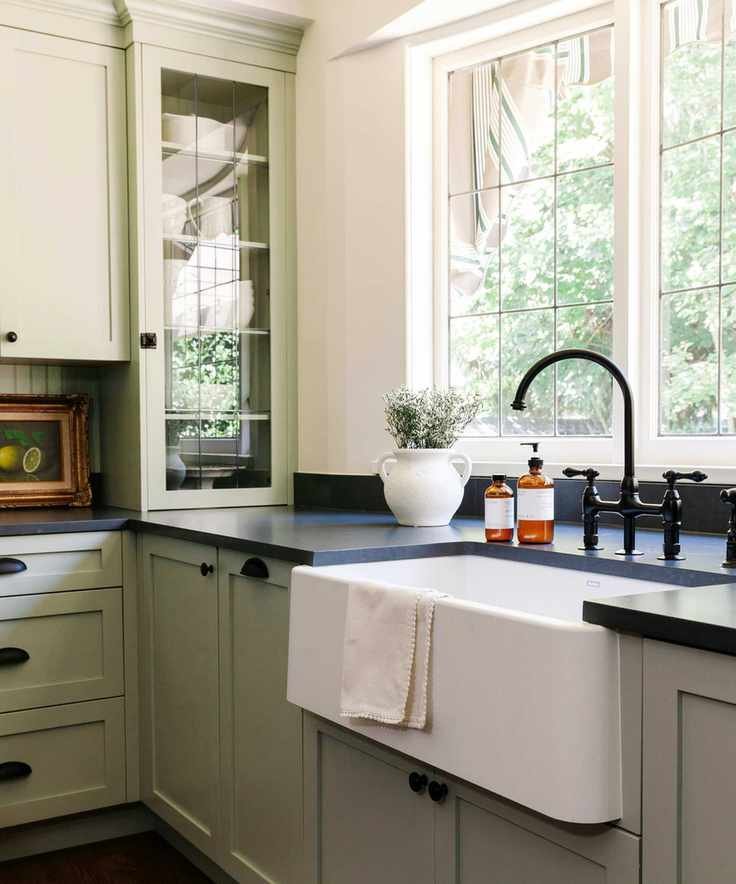 A sage green kitchen with large windows