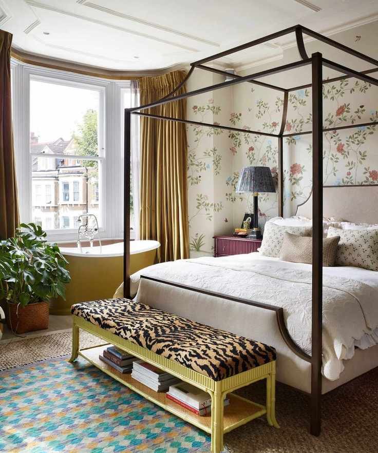 A vibrant room with a floral mural, a four-poster bed, and a stylish yellow bench at the foot