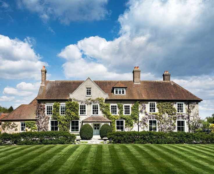 An example of front garden ideas showing a large country home with a neat lawn, low level hedging and ivy on the house