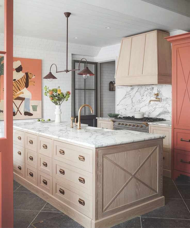 A marble, wood and terracotta kitchen with a large wooden island with marble countertop, marble backsplash, gold taps and terracotta accents on doors, cabinets and artworks.