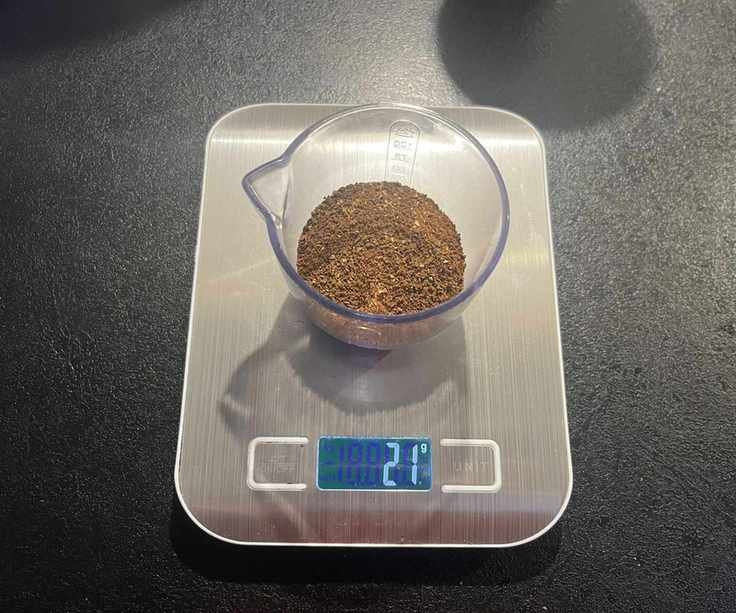 Medium ground coffee beans in a clear plastic container on digital weight scales.