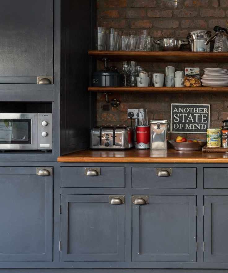 Navy blue kitchen with exposed brick wall, shelving and microwave