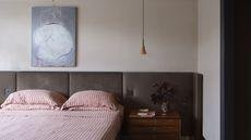 A mid-century style bedroom with a large brown headboard, a wooden nightstand, and a red and white striped bedding set