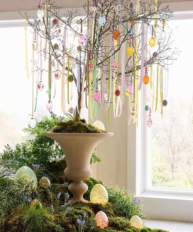 Large tree potted in an urn with a branchy tree decorated for Easter with eggs and ribbon with the base surrounded by moss and eggs