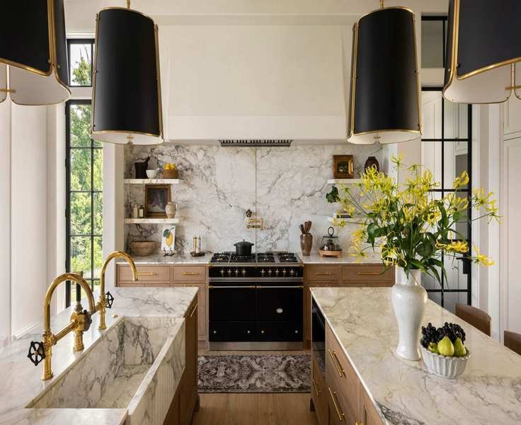 White kitchen with mix of white and wood cabinets. The countertops are marble and the lights above are dark black shades with gold accents that matches the fixtures and hardware in the