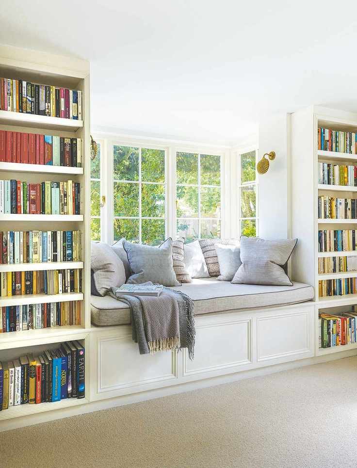 library with bay window seat and fitted bookshelves either side with view of garden