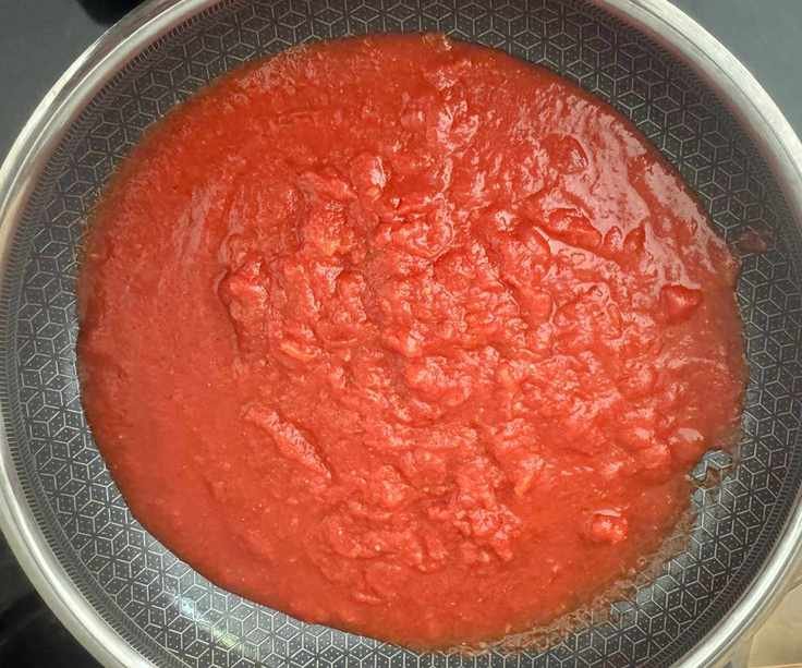 Red tomato sauce in a black lined stainless steel frying pan, viewed from above.