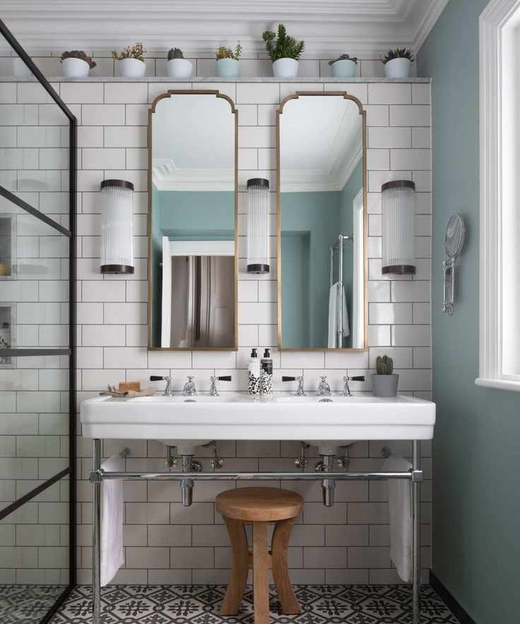 A white bathroom with gold mirrors, patterned floor tiles, and house plants on a high shelf