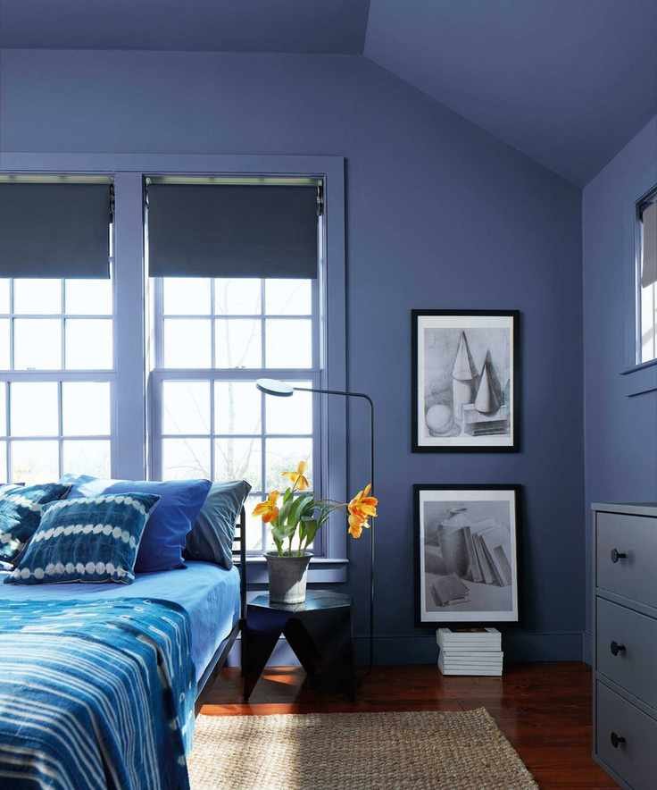 Blue bedroom with blue painted walls, blue duvet and pillows on bed, angular bedside table, jute rug and blue drawers