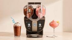 A black Ninja SLUSHi twist machine, with two dispensers, one filled with cola slush, the other with a pink slush. A glass of each on either side.