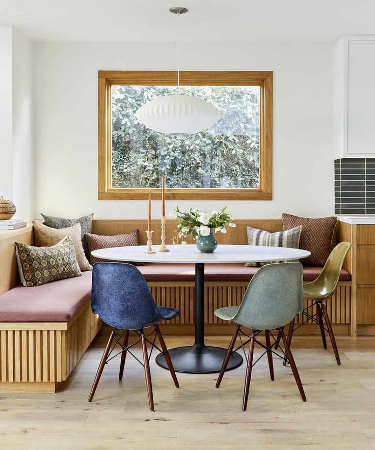 A small dining room idea with a white oak dining bench and colored chairs with white walls