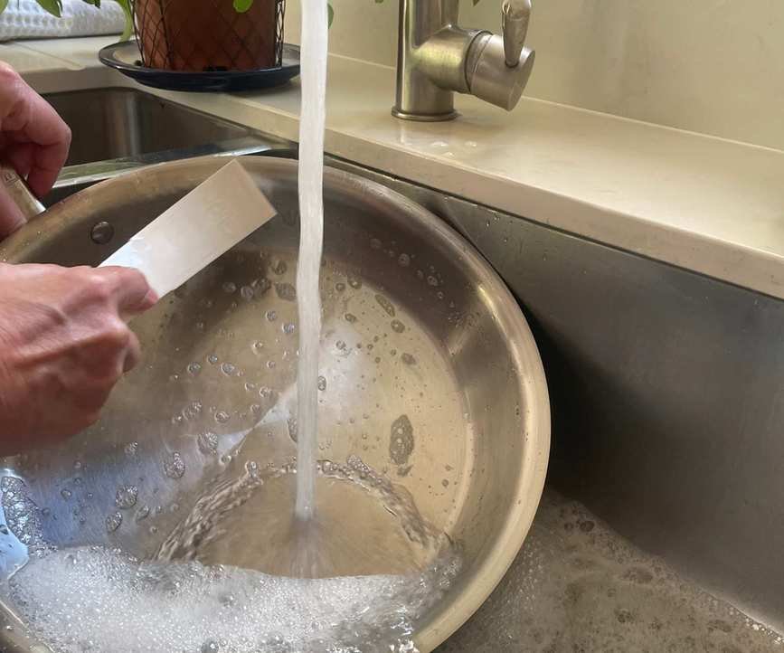 Made In stainless steel pan being hand washed with a scrubbing brush in a sink.